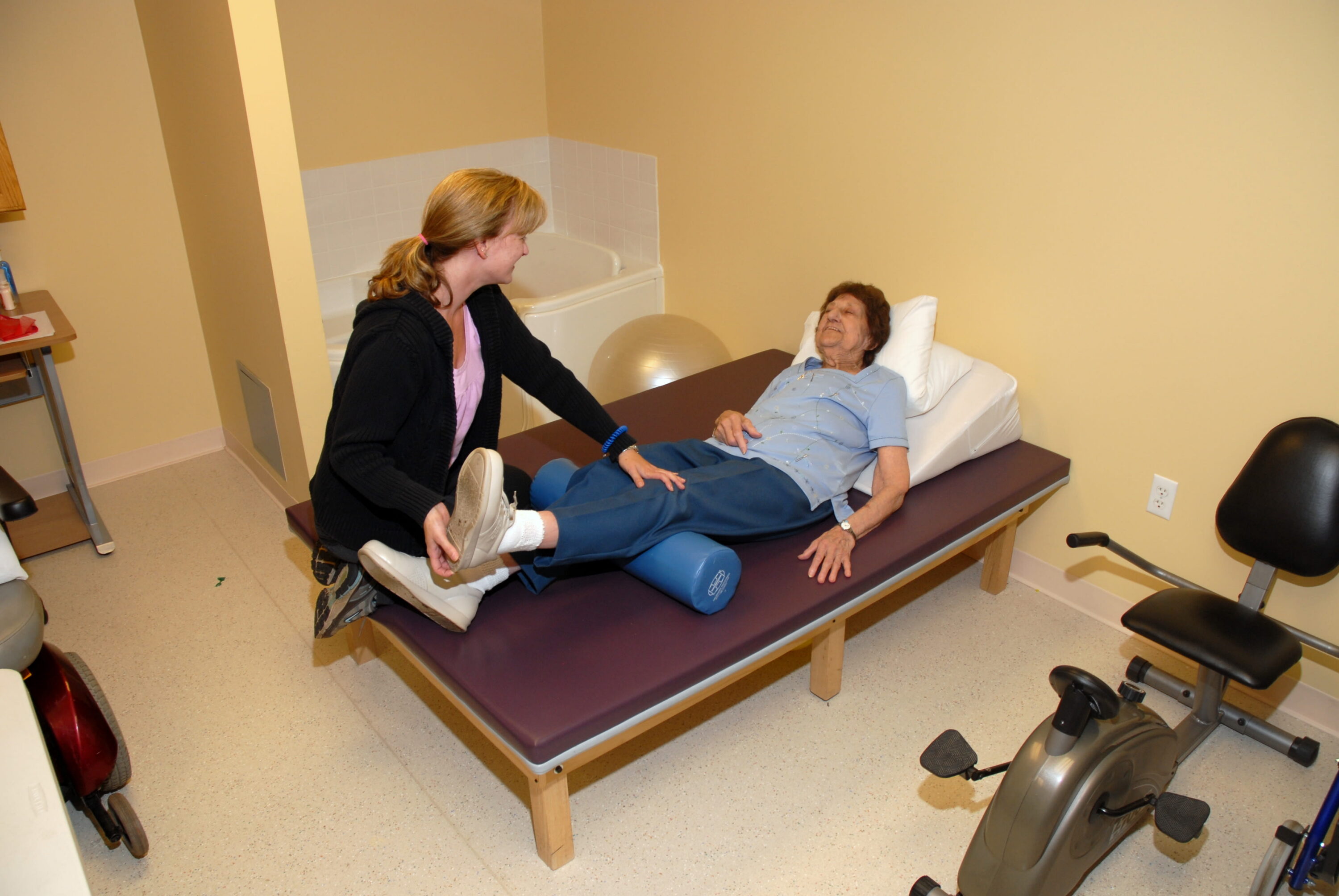 Therapist assisting elderly woman with leg exercise