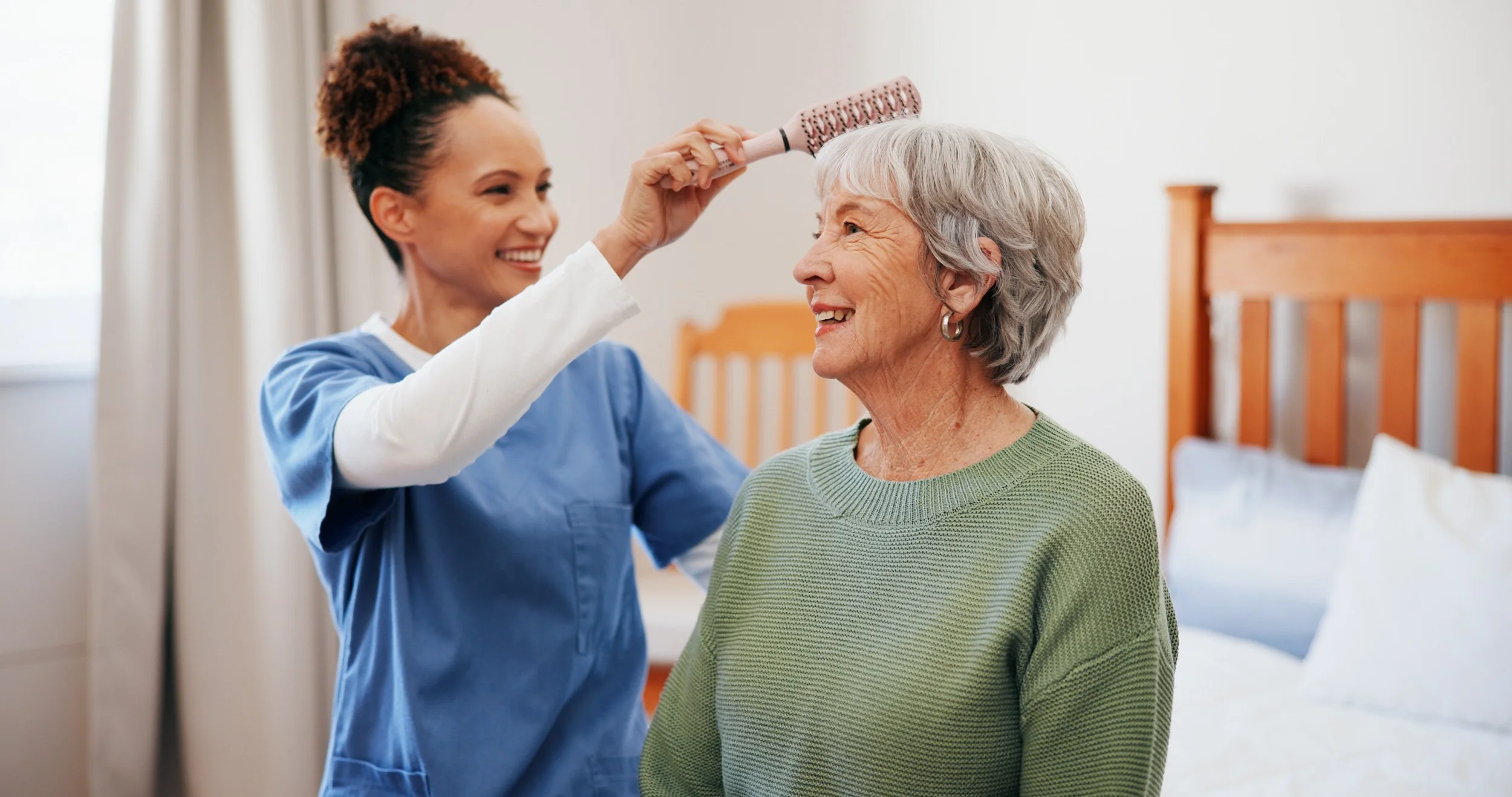 Caregiver brushing elderly woman's hair in bedroom