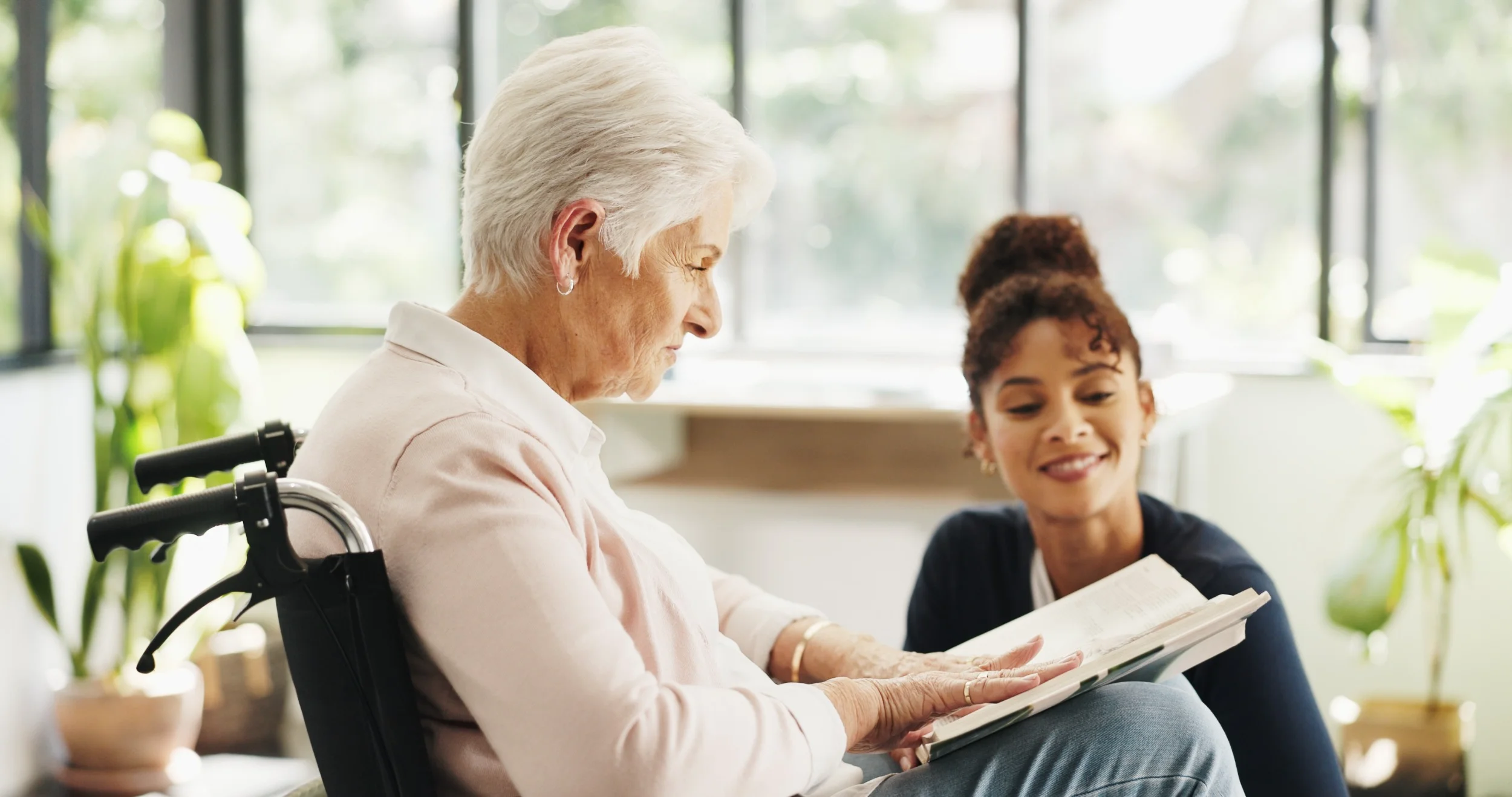 Elderly woman in wheelchair reading with caregiver