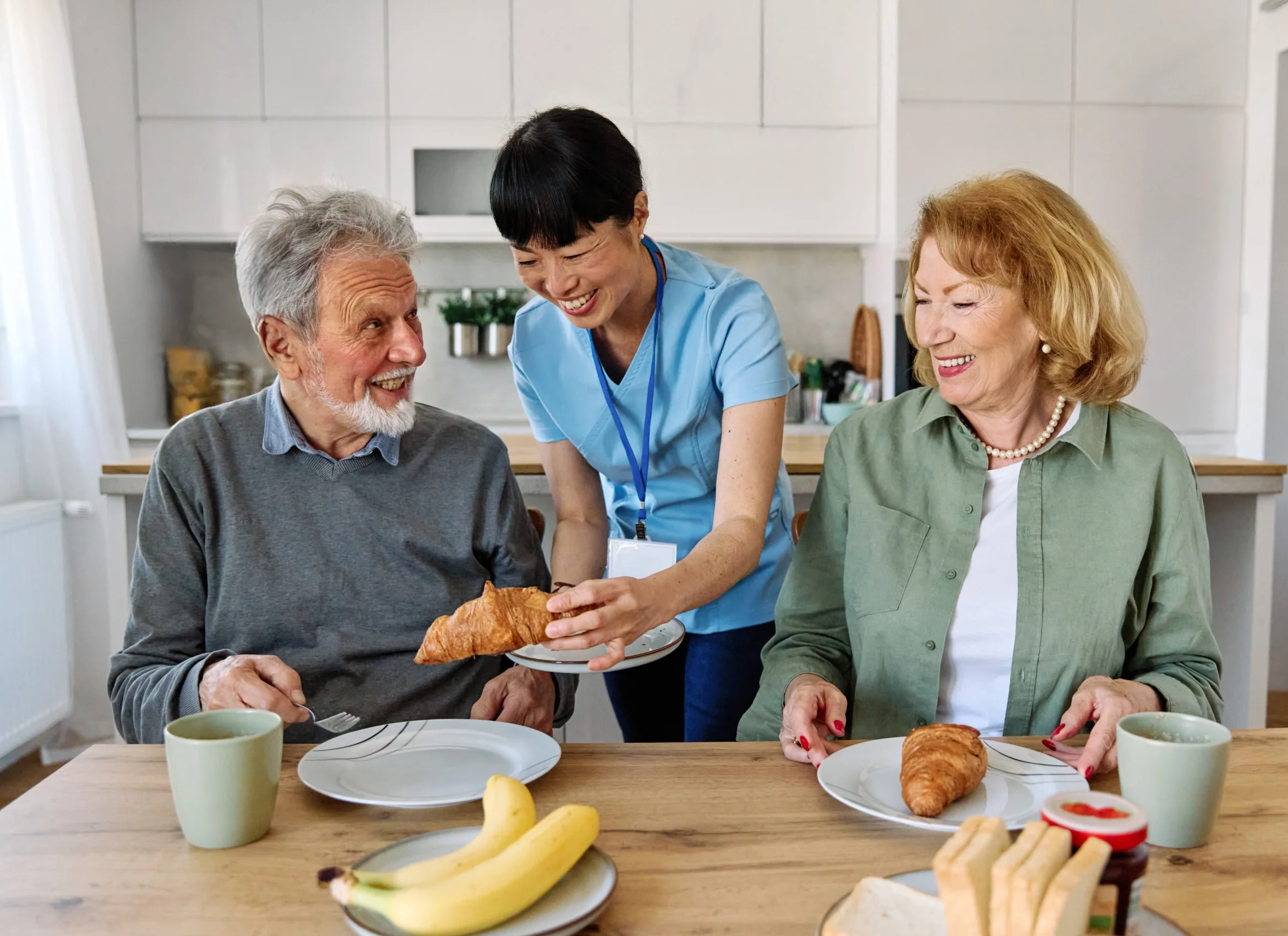 Caregiver serving breakfast to smiling elderly couple