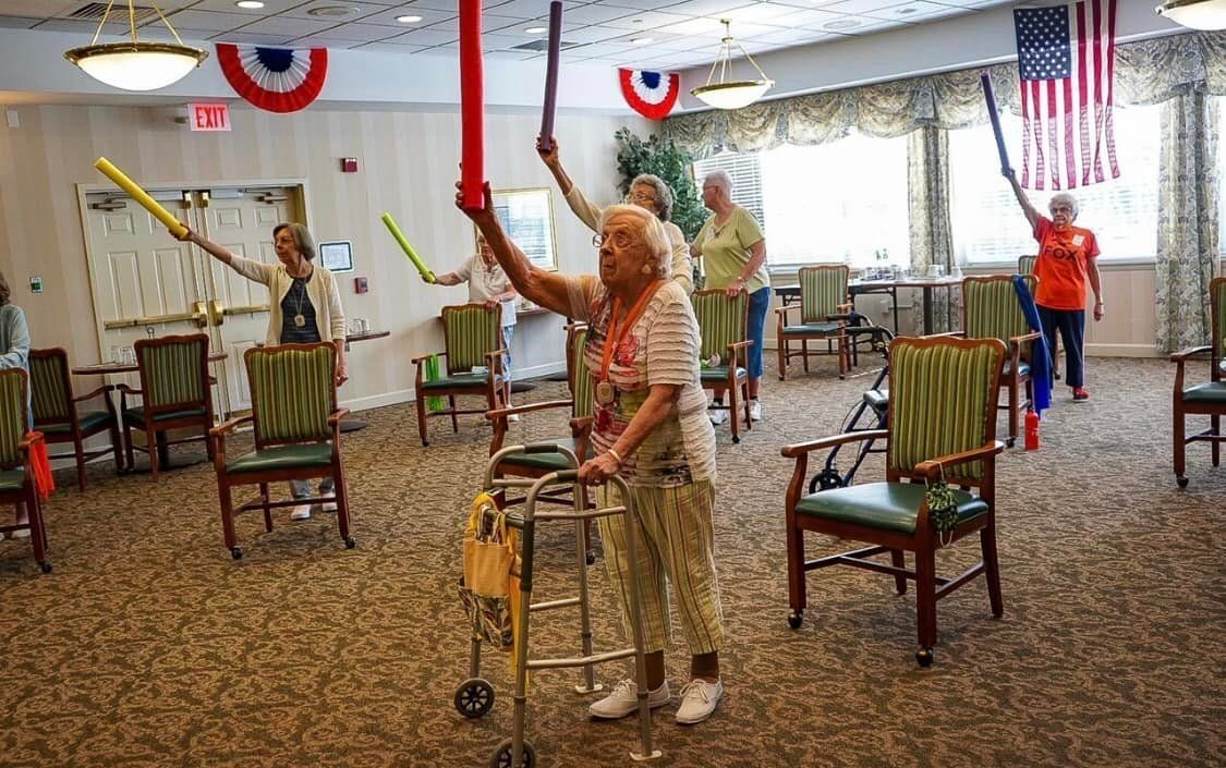 Seniors exercising with pool noodles in community room