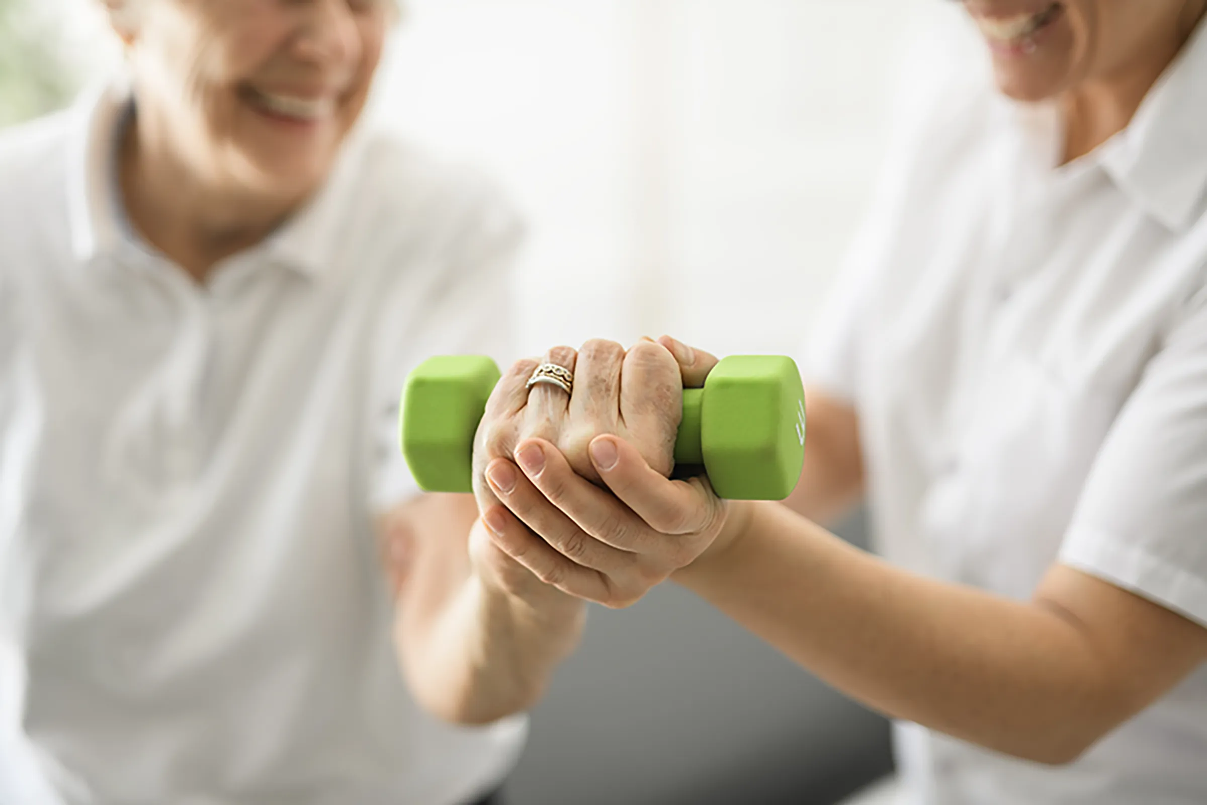 Caregiver assisting senior with green dumbbell exercise