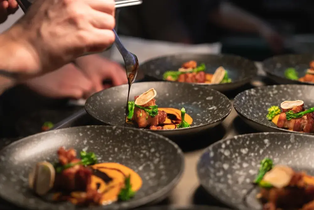 Chef drizzles sauce over gourmet plated meat dishes