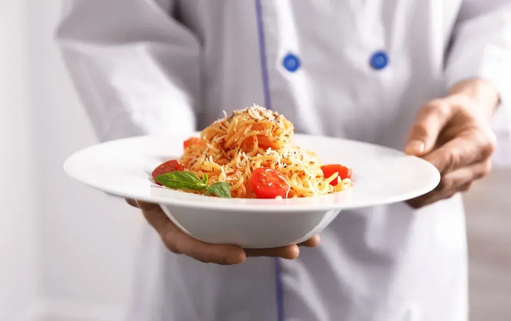 Chef holding plated spaghetti with tomatoes and basil